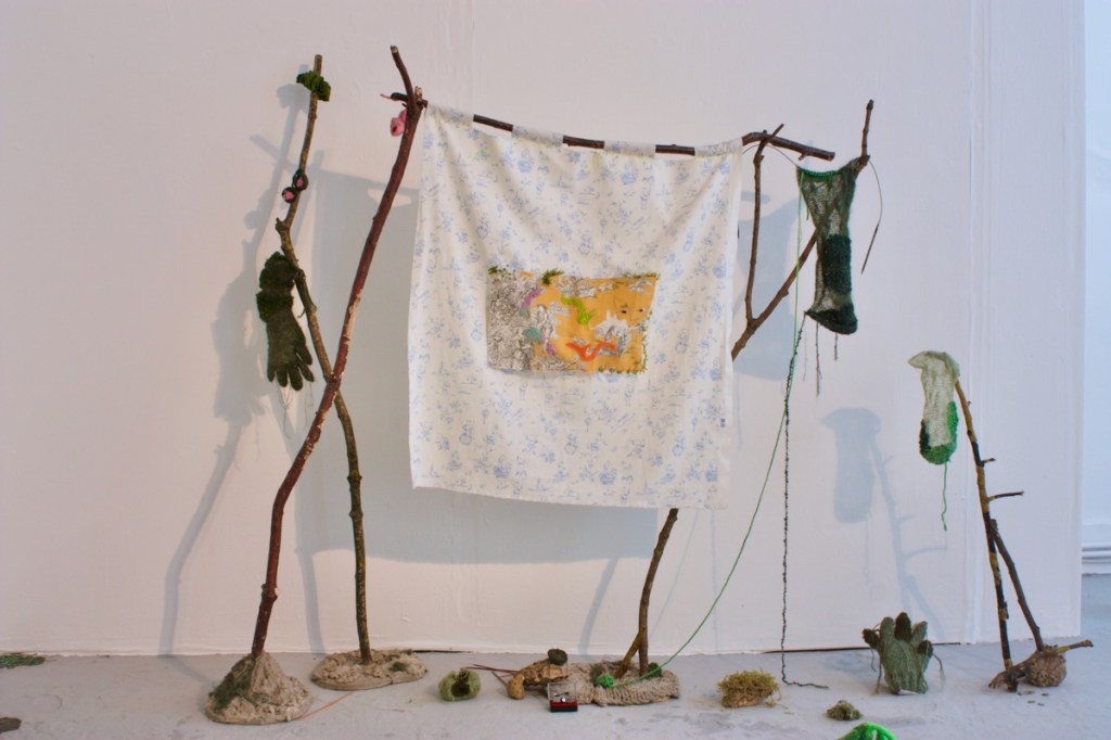 fabric hanging made from reclaimed Chinoiserie and toile, balanced on foraged sticks set into concrete & wool bases, surrounded by various pieces of green knitting 