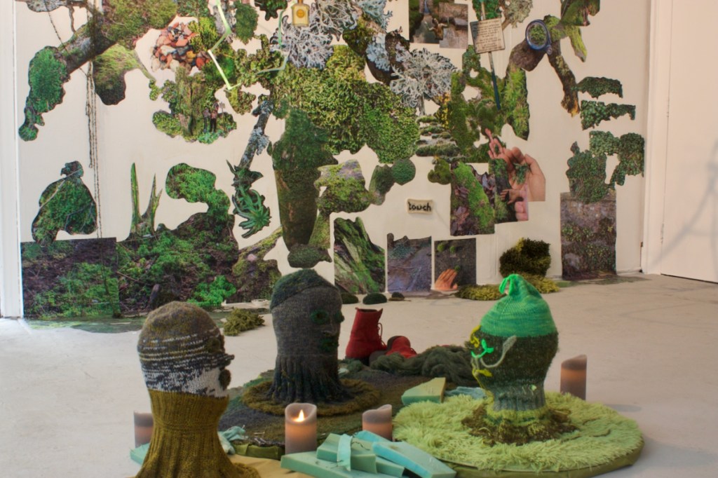view of 3 knitted heads on cushions surrounded by LED candles and mossy mural in background