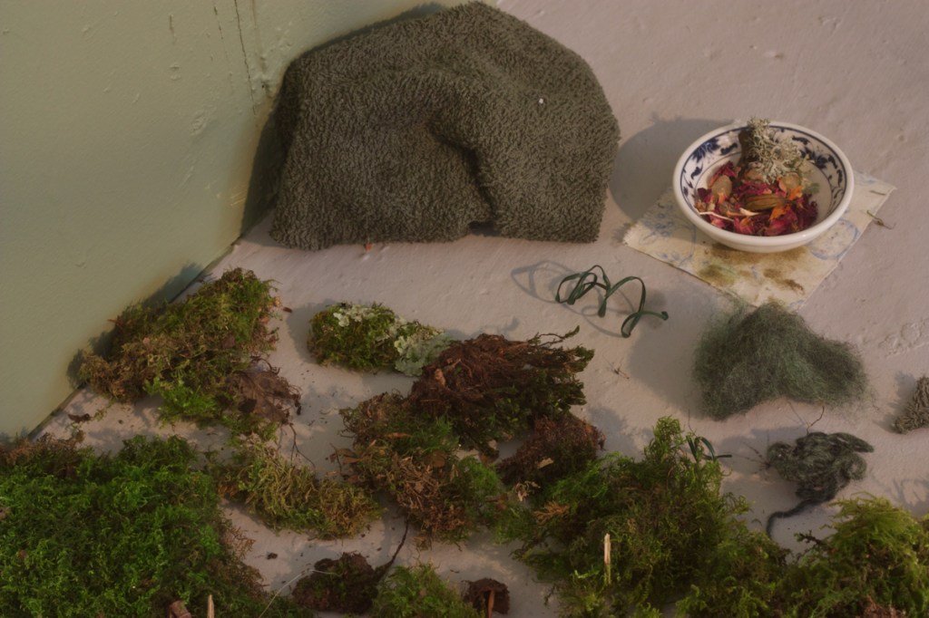 Detail of real mosses, dark green terrycloth, twisted garden wire, blue& white dipping dish with pomander resting on Chinoiserie scrap stained with oakmoss absolute.