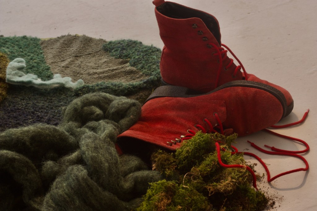 Close-up of moss, dark green wool roving, moss-like cushion, and red suede boots