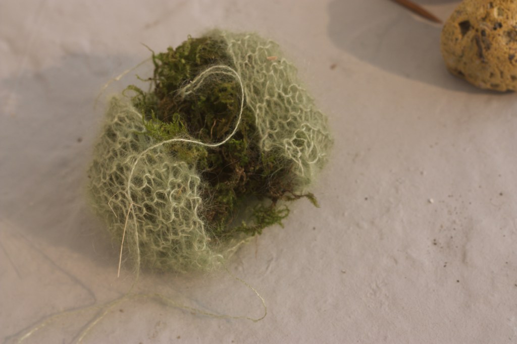 detail of pale green knitted broken sphere made of mohair, enclosing a dark mossy heart