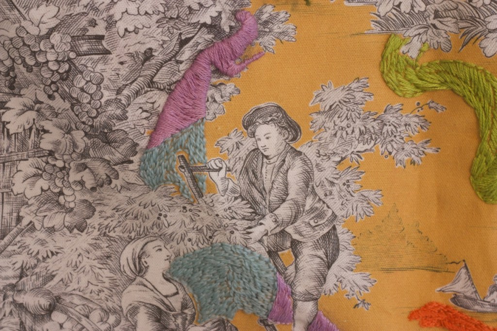 close-up detail of embroidered toile with kicking legs, fruit tree, and fruitpicker