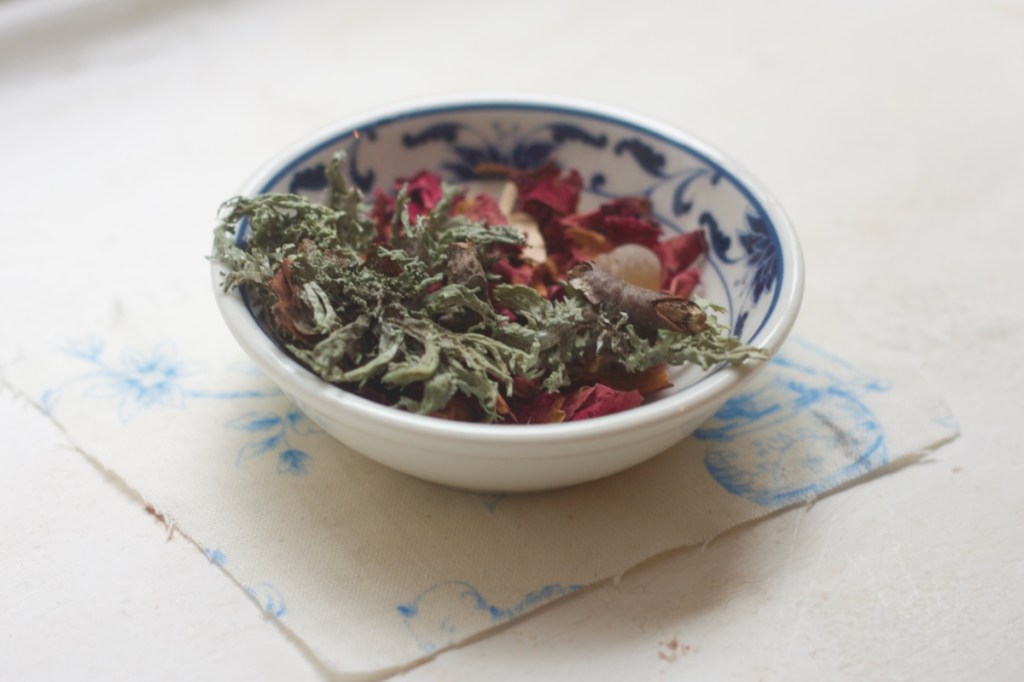 Tiny blue and white dipping dish with plague pomander + the addition of oakmoss, sitting on top of small square of Chinoiserie fabric