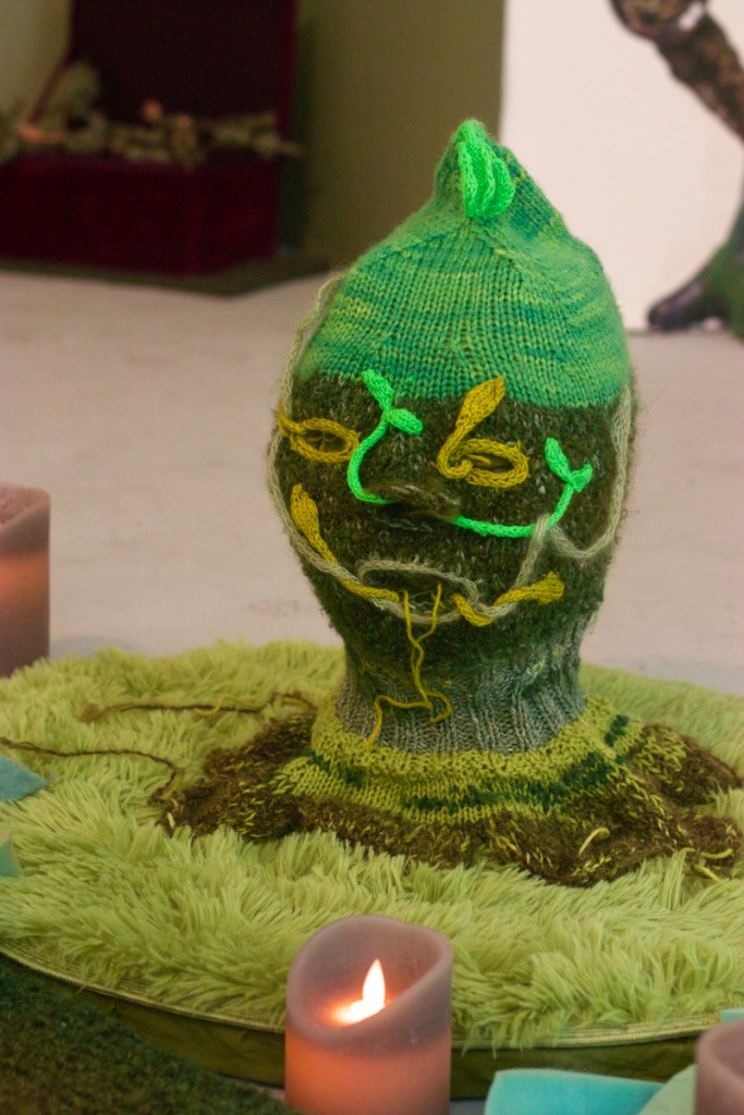 green knitted head with bright green sprouts coming out of its face holes